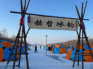 Colorful tents on a snowy field with a wooden arch bearing Chinese text. People walk nearby. Clear sky and trees in the background.