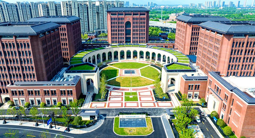 Aerial view of a red brick campus with a courtyard, green roofs, and surrounding skyscrapers. Bright, sunny day creates a vibrant mood.