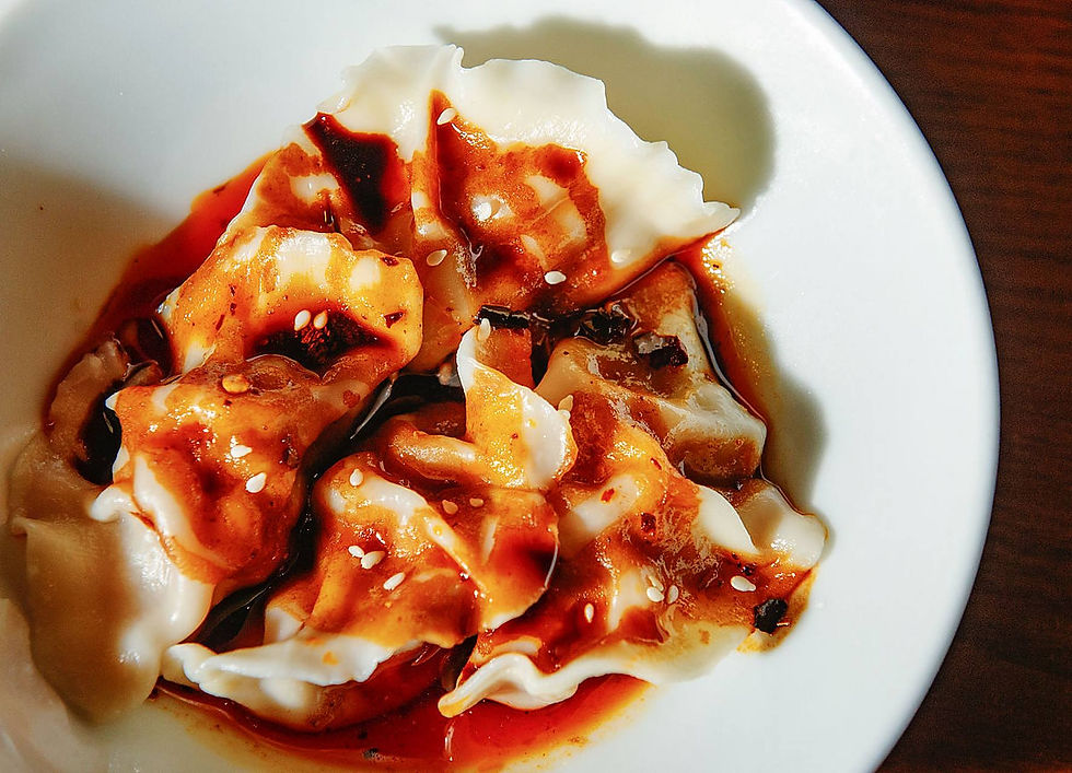 Dumplings in a white bowl covered with spicy red sauce and sesame seeds, creating a vibrant and appetizing appearance.