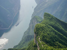 River winding through green mountains; a boat travels along the water. Sunlight reflects on the surface, creating a serene atmosphere.