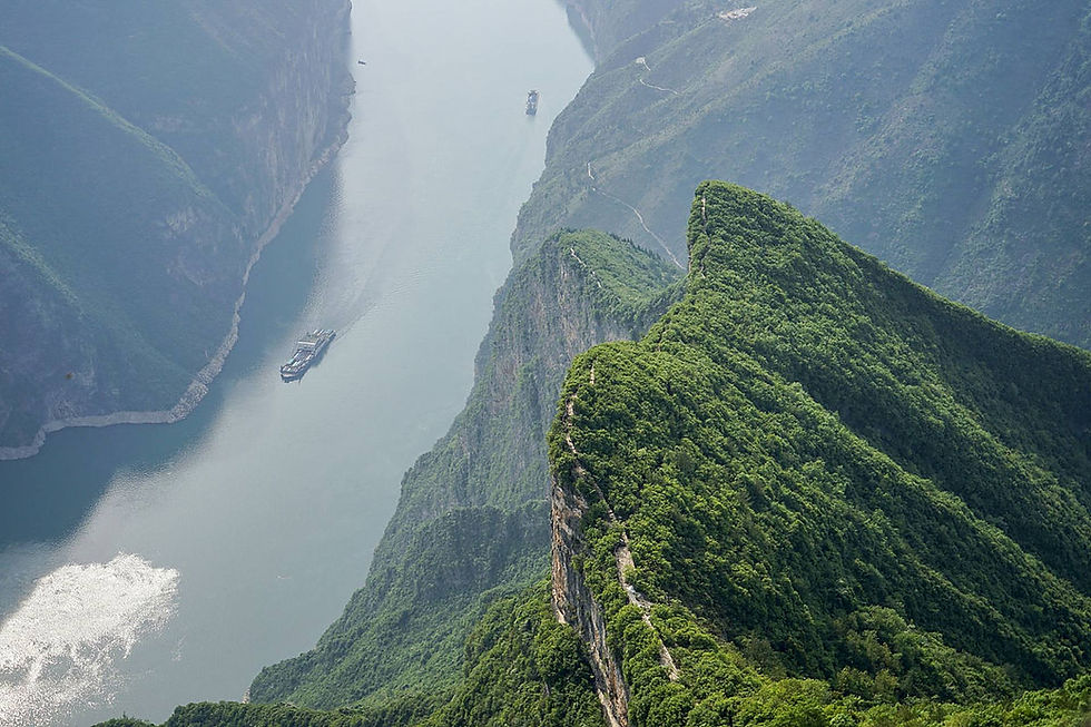 River winding through green mountains; a boat travels along the water. Sunlight reflects on the surface, creating a serene atmosphere.