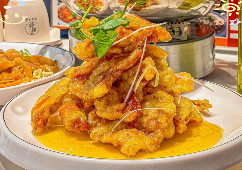 Stack of crispy fried shrimp with garnish on a white plate, drizzled with golden sauce. Side dish and text in background. Bright setting.