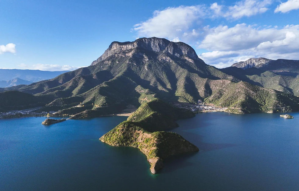 Mountain landscape with a huge peak and smaller hills surrounded by blue lake under a clear sky. The scene is calm and expansive.