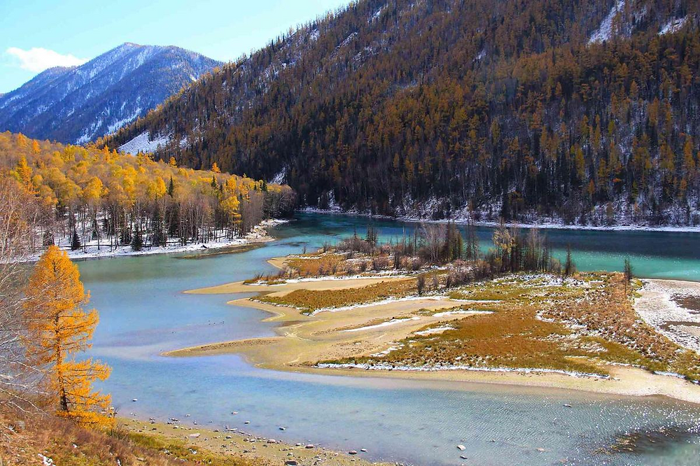 Mountain valley with a winding blue river, golden autumn trees, and snowy patches. Majestic and serene landscape under a clear sky.