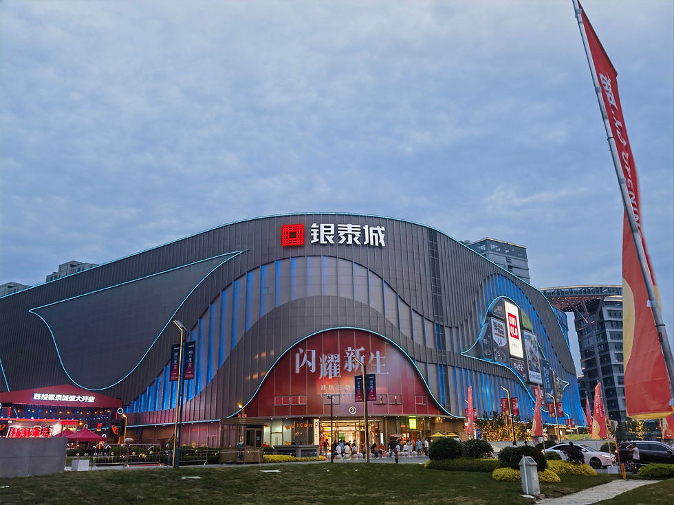 Modern shopping mall with wavy design and blue neon lights. Red signage displays Chinese characters. People gather at entrance, sky above.
