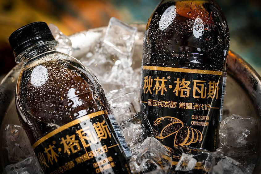 Two black bottles with yellow text in Chinese are nestled in ice in a metal bucket. Bottles have condensation, creating a refreshing look.
