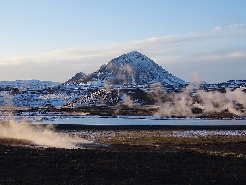 Snow-covered mountain with steam rising from the ground, against a clear blue sky. The landscape is serene and vast, with a tranquil mood.