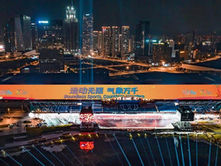 Night cityscape with a lit stadium displaying "Boundless Sports" in both English and Chinese. Bright city lights and skyscrapers in the background.