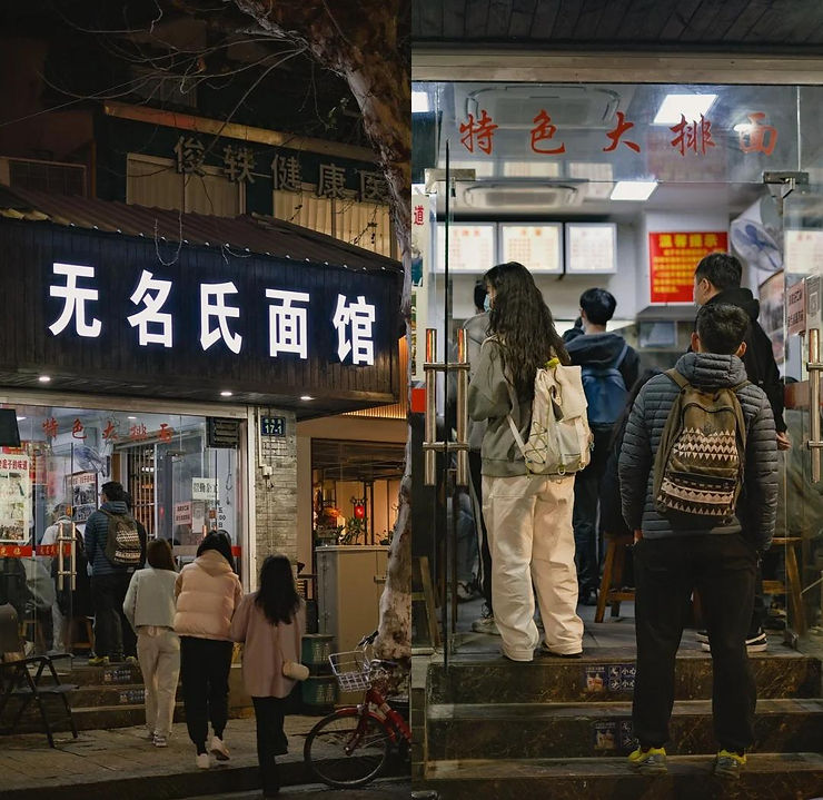 People in warm clothing enter a dimly lit noodle shop with a neon sign in Chinese, creating a cozy, inviting street atmosphere at night.
