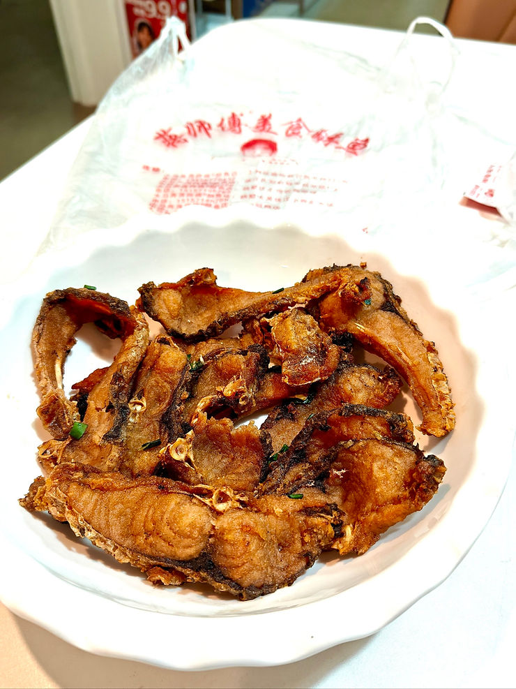 Crispy fried fish pieces on a white plate with a plastic bag featuring red Chinese text in the background, creating a homey feel.