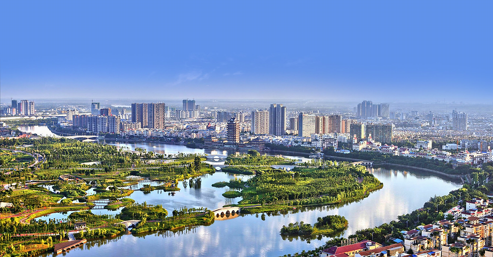 Cityscape view of a river with lush greenery, modern buildings, and bridges under a clear blue sky, evoking a serene urban vibe.
