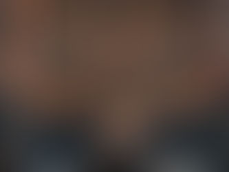 Rows of wooden benches face a seated Buddha statue in a dimly lit temple. A wall filled with small, intricate statues creates a peaceful atmosphere.