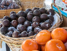 Baskets of frosty black and orange fruit on display at an outdoor market. Snow dusts the fruit, set against baskets and market signage.