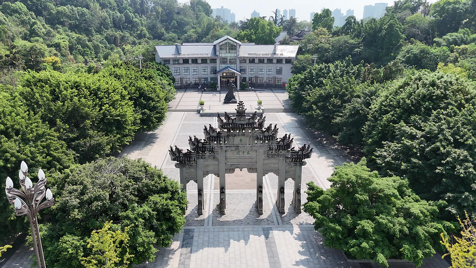 Aerial view of an ornate stone gate, a statue, and a building amid lush green trees under a clear sky.