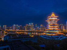 City skyline at night with illuminated traditional pagoda and colorful skyscrapers. A river reflects the vibrant lights, creating a lively atmosphere.