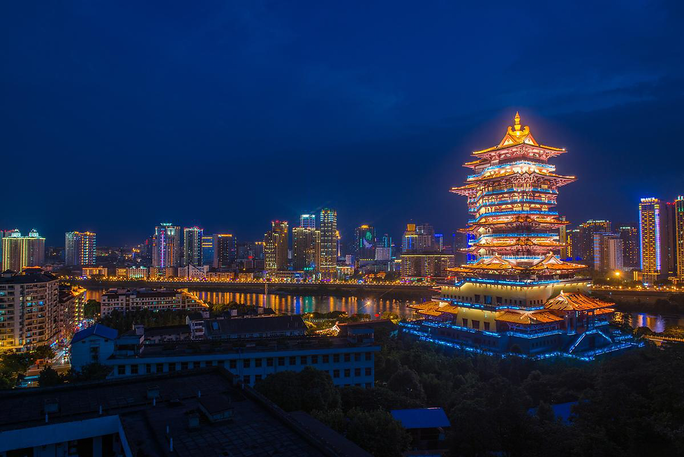 City skyline at night with illuminated traditional pagoda and colorful skyscrapers. A river reflects the vibrant lights, creating a lively atmosphere.
