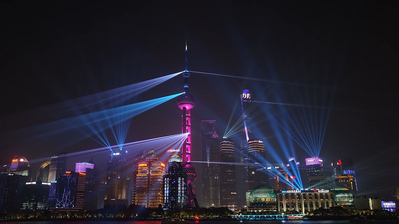Shanghai skyline at night with colorful laser beams illuminating skyscrapers, including the Oriental Pearl Tower. Bright city lights and dynamic atmosphere.