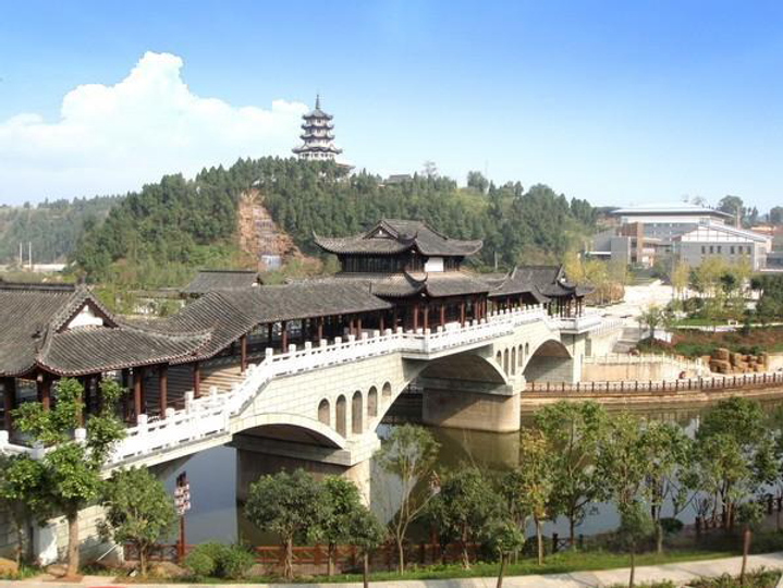 Traditional Chinese bridge with ornate roof spans a river. Lush greenery, distant pagoda, and blue sky create a serene landscape.