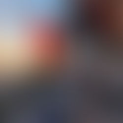 Two people sitting on a wooden path with a guitar, surrounded by red lanterns. Sunset over a river and bridge in the background. Tranquil mood.