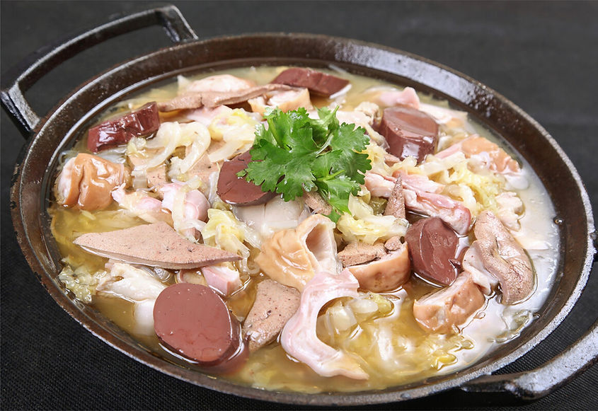 Soup with various meats and vegetables in a metal pot, topped with cilantro. Dark background, the dish looks savory and vibrant.