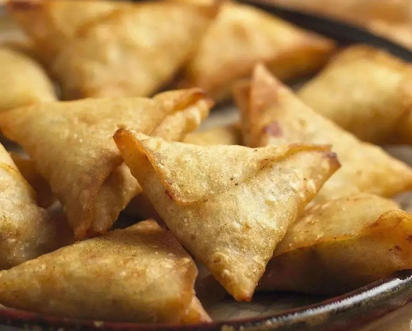 Golden-brown triangular pastries stacked on a plate, crispy texture visible. Warm, inviting atmosphere. No text present.
