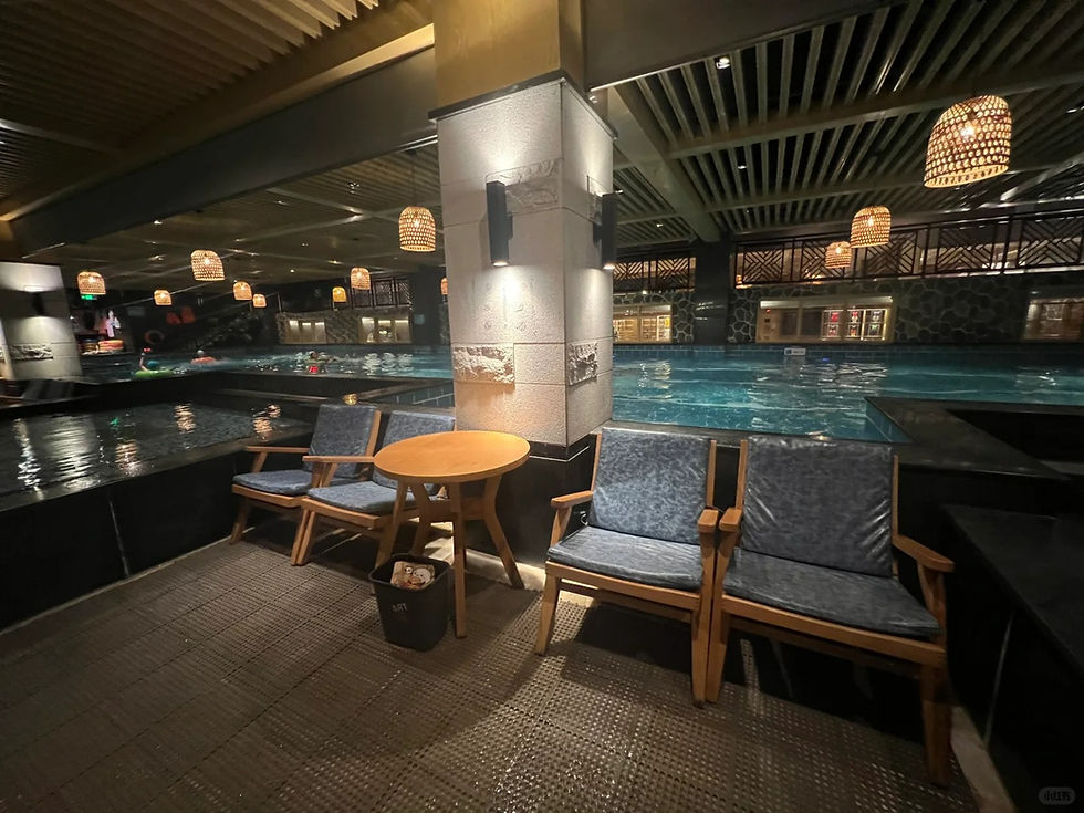 Indoor pool area with blue water, wooden chairs, a small table, and wicker lamps. The space has a calm, relaxed ambiance.