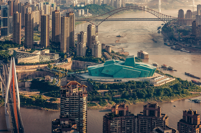 Aerial view of a cityscape with tall buildings, a turquoise-roofed structure, and a river with bridges. Warm lighting, urban setting.