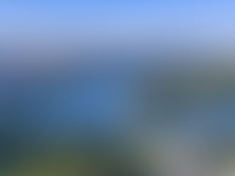 Aerial view of a city by a winding river, surrounded by lush greenery. Tall buildings and clear blue skies create a tranquil urban landscape.