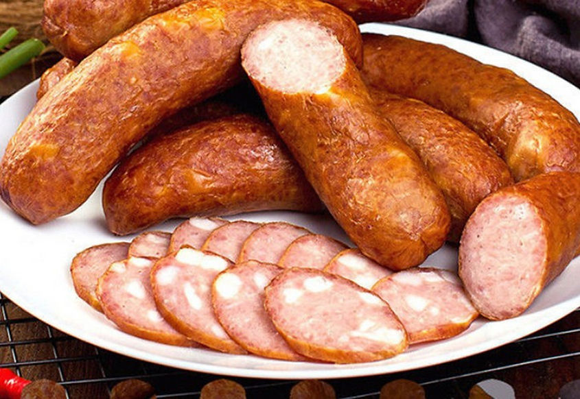 Sliced sausages on a white plate, showcasing a rich, brown color and juicy texture. Sausages are placed on a rustic wooden surface.