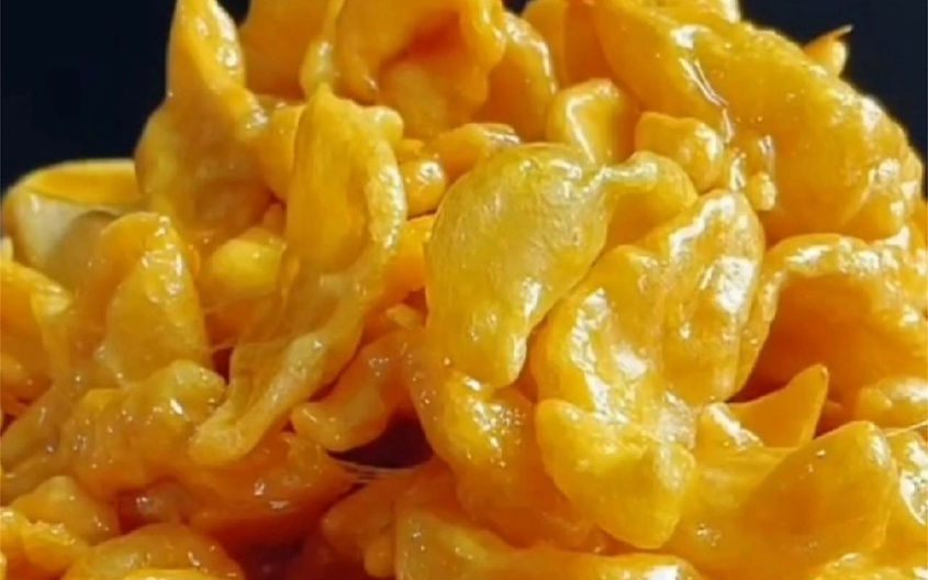 Close-up of caramel-coated cornflakes in a glossy, golden-yellow hue against a dark background, creating a sweet and indulgent mood.