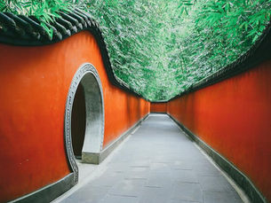 Traditional Chinese gate with red walls and dark tiled roof. Stone lion statues flank the entrance. Trees and intricate patterns adorn the scene.
