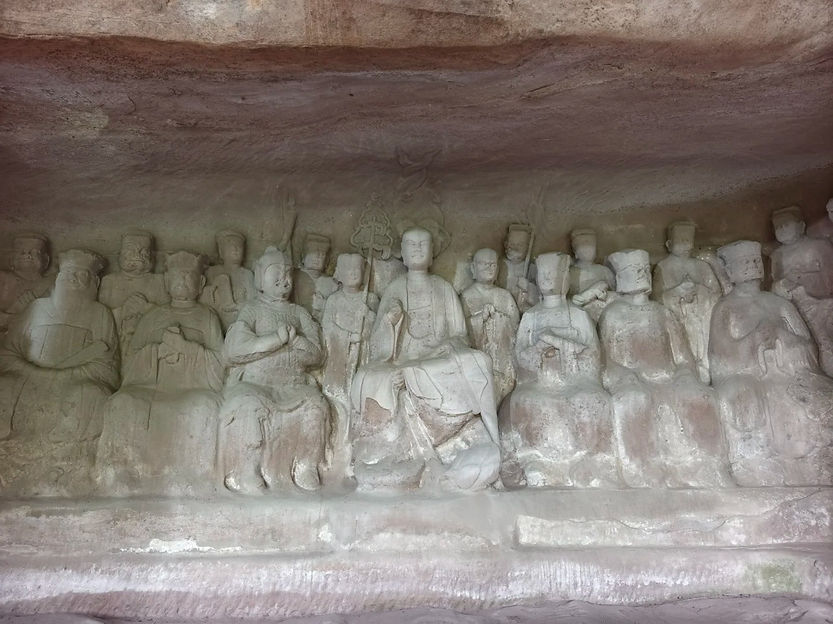Stone carvings of seated figures in a cave, featuring intricate details. The figures appear solemn, set against a textured stone backdrop.