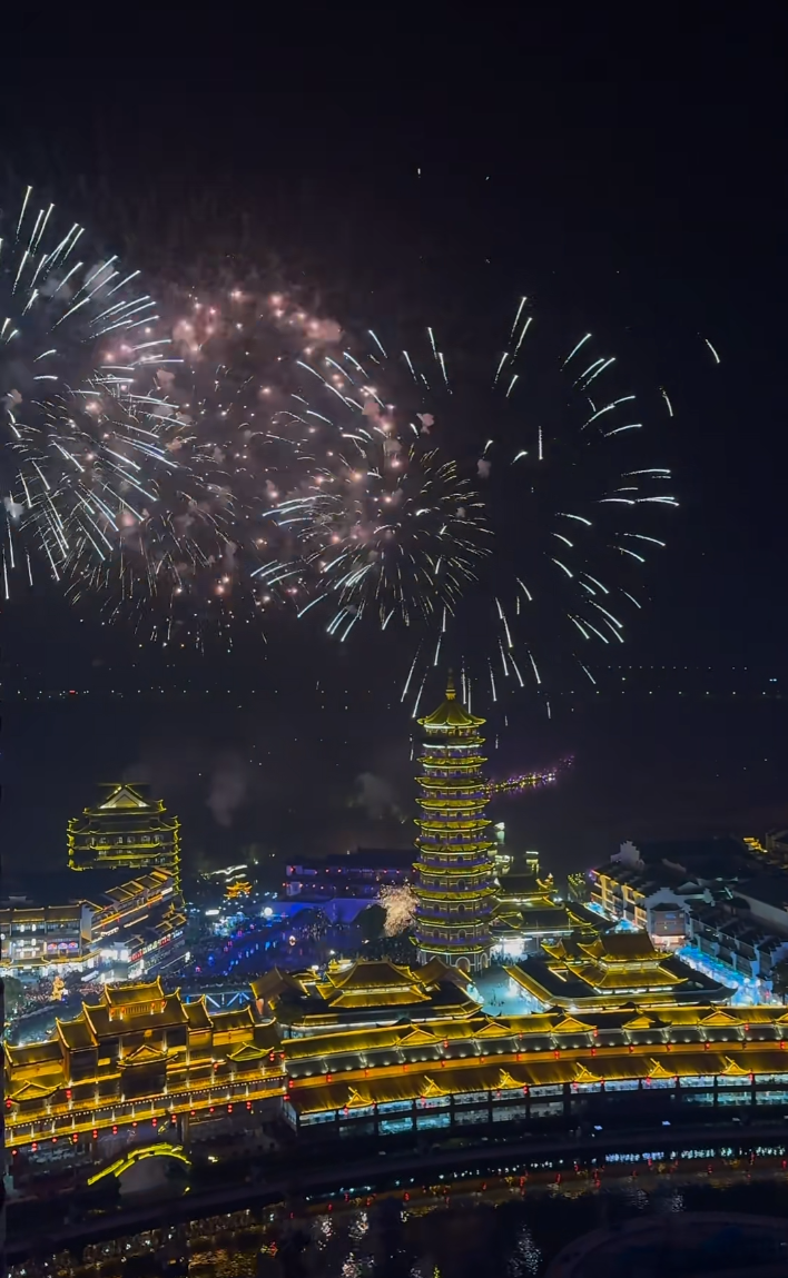 Fireworks light up the night sky over an illuminated pagoda and traditional Chinese buildings, creating a festive and vibrant scene.