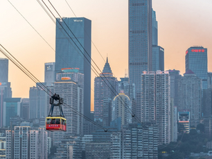 Red cable car traverses against a city skyline at sunset, with tall skyscrapers and visible text on buildings in the background.