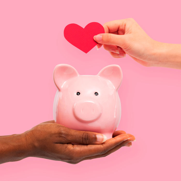 Creating Customer Loyalty, Photo of hand holding piggy bank and other hand depositing heart.