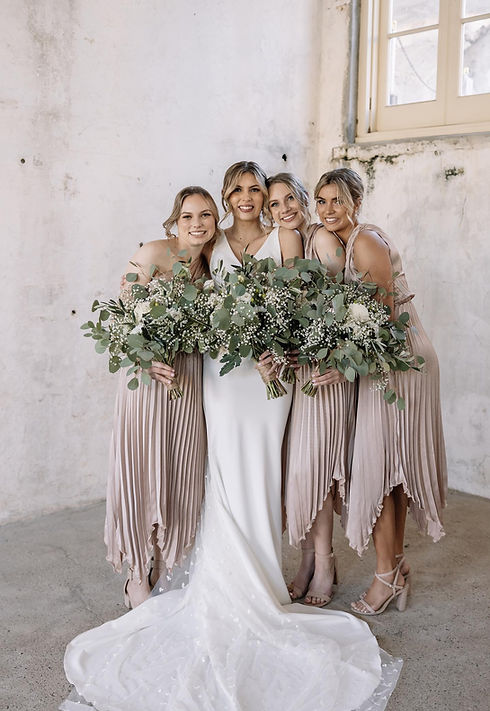 Four women in colorful dresses stand together, smiling and posing for the camera in a bright outdoor setting.