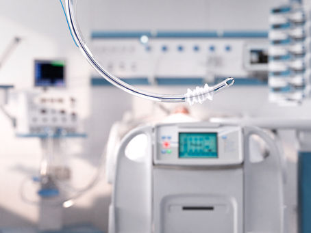 Medical tubes with blue and yellow connectors float in a hospital room, with a dialysis machine and monitors in the blurred background.