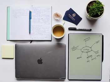 flat lay of a computer, notebook, tablet with writing, coffee cup, plant, and pen
