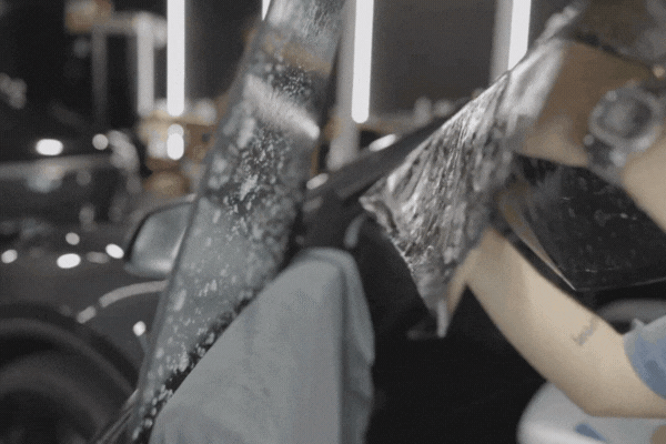 Close-up of a professional applying wet adhesive window tint film to a car door window, with visible water droplets on the glass during installation.