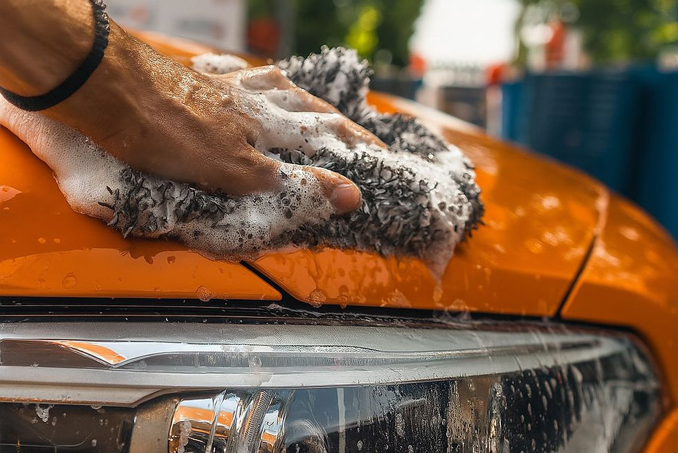 A person hand-washing an orange vehicle with a soapy microfiber mitt, gently cleaning the hood just above the headlight. This image highlights how regular, careful washing is key to maintaining the scratch-resistant benefits of Paint Protection Film.