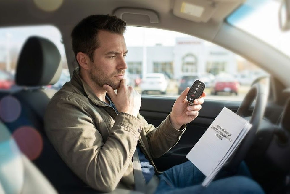 Driver sitting in a vehicle and reviewing a key fob while holding a vehicle warranty booklet. The image relates to questions about aftermarket remote start installation and how it can affect factory warranty coverage.