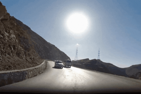 Dashcam view of cars driving on a winding mountain road under intense sunlight, highlighting environmental exposure like UV rays and road debris that can affect vinyl wraps.