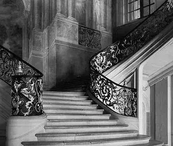 Grand black-and-white staircase with ornate wrought-iron railings in a stately interior, curving upward through tall windows.
