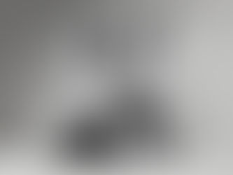 A person in beige outfit stands atop a colorful pile of clothes, arms raised with cheer. Neutral background highlights the vibrant textiles.