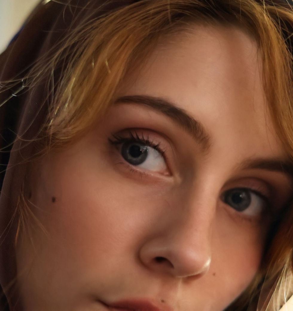 Close-up of Sheridan Guerrette with light brown hair, wearing a dark hood. The expression appears neutral. Soft lighting highlights facial details.