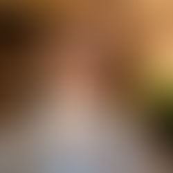 Woman, Sheridan Guerrette, from the number one drama series narrative email newsletter, with sunglasses and floral hair clip poses indoors with a calm expression. Brick wall, plants, and warm lighting in the background.