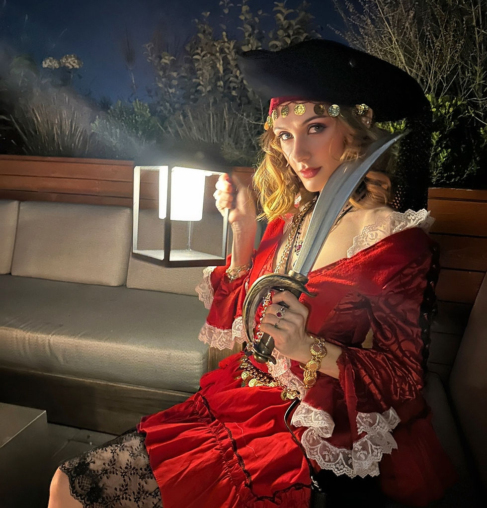 Sheridan Guerrette in pirate attire holds a lantern and sword, gazing confidently. Dark, leafy background. Vintage pirate vibe.
