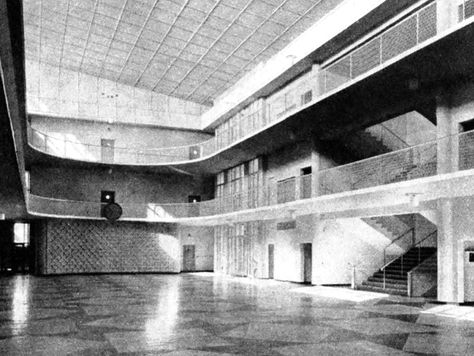 Spacious, empty indoor hall with multi-level balconies and geometric floor patterns. Bright lighting and minimalist design create a serene mood.