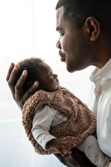 Père tenant son nouveau-né, regardant avec tendresse, en arrière-plan clair.