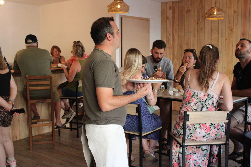 Baptiste portant une assiette de pizza dans la salle du  restaurant La Cabane, animé rempli de clients lors de l'inauguration
